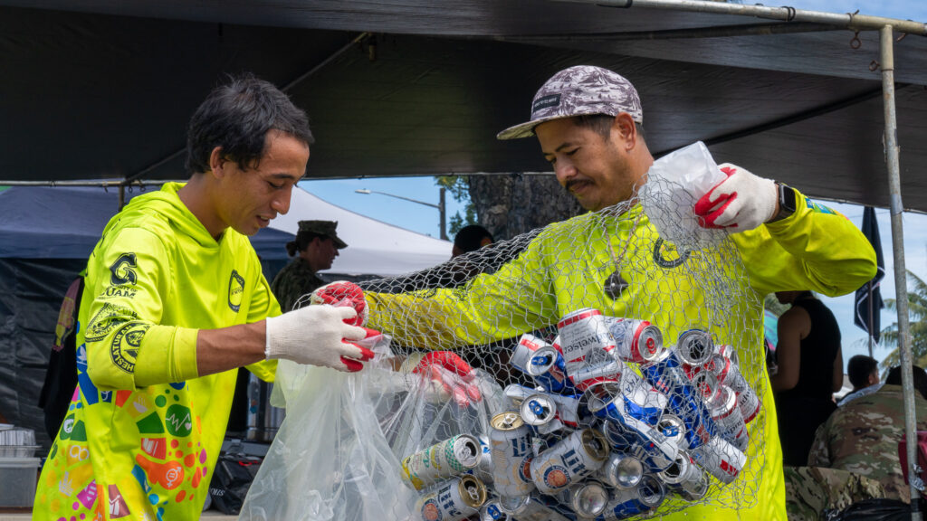 Gideon Tyquienco and Matthew Pangelinan transfer aluminum from a can bin into a trash bag.