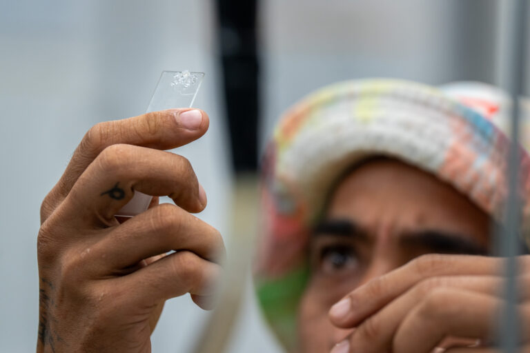 A close-up of man holding small glass slide containing a tiny specimen.