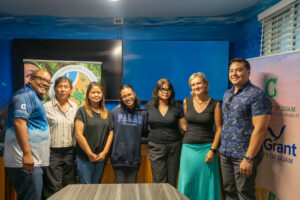 A group of seven people, including Navigating Home Fellow Kira Reklai, stand smiling side-by-side indoors for a photo following a final fellowship presentation.