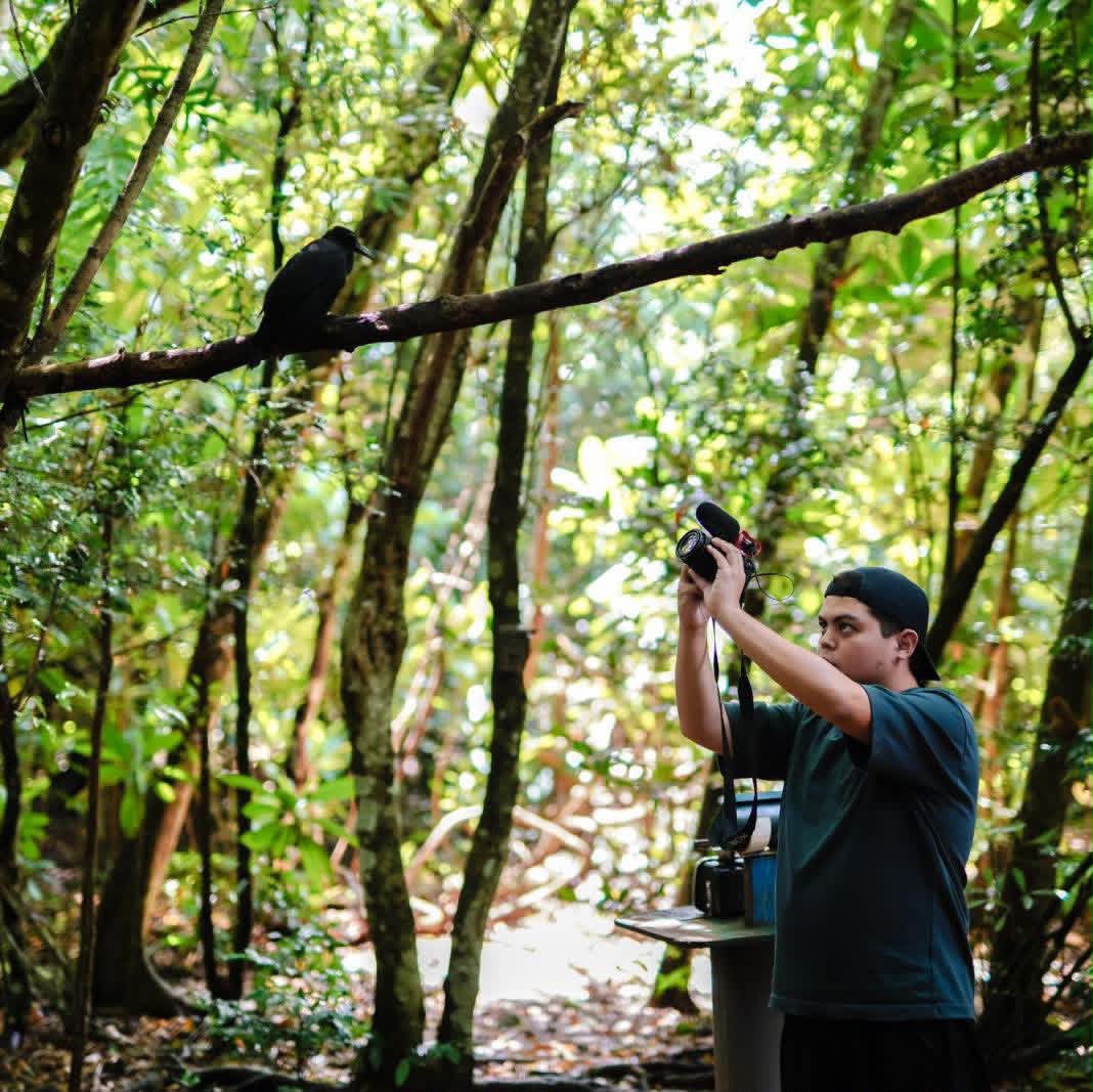 Thomas Manglona holds a camera up to take a photo while in the jungle.